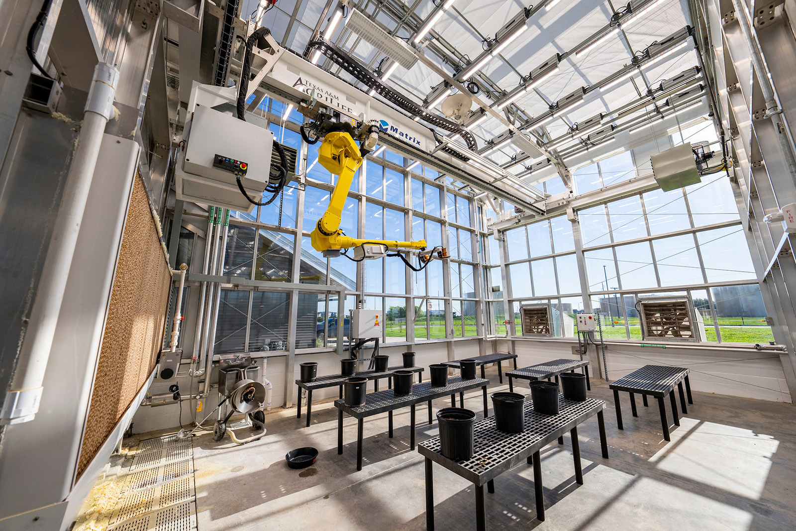 Wide shot of glass greenhouse interior with robot arm and track system attached to ceiling.